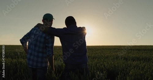 A man and his son watch the sunrise over a wheat field together. Farmers in the field and family business
