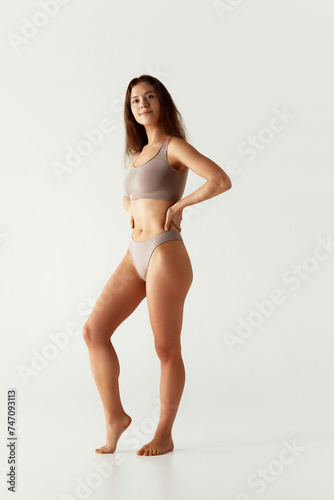 Full-length portrait of beautiful brunette woman posing in chocolate color underwear against grey studio background. Concept of beauty treatments, dieting, female health, spa procedures. Ad