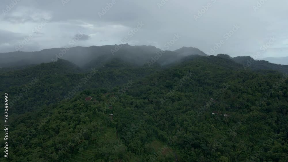 Aerial view of fog that slowly shroud the forests in the mountain range in the morning. Natural endless woodland of Indonesia.