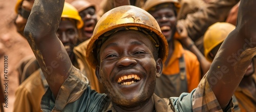 A crowd of happy men wearing hard hats raise their arms in the air at a festival event, smiling and laughing in fun and excitement.