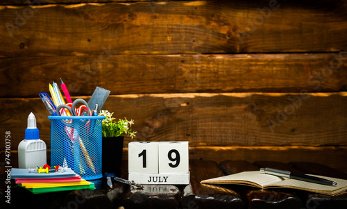 July calendar with number  19. Office background with pencils pens and ruler copy space. Beautiful background planner calendar on a brown wooden background, space for text. photo