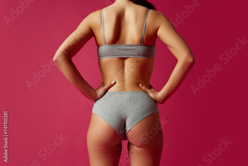 Rear view, cropped portrait of young woman holds hands on hips against magenta studio background. Anti-cellulite. Concept of beauty treatments, dieting, female health, femininity, plastic surgery.