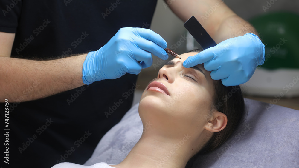 A cosmetologist marks with a pen the site of a beauty injection in the forehead of a beautiful patient. Concept of preparing for an injection of a beautiful young woman. A cosmetologist marks with a pen the site of a beauty injection in the forehead of a beautiful patient. Concept of preparing for an injection of a beautiful young woman.