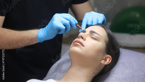 A cosmetologist marks with a pen the site of a beauty injection in the forehead of a beautiful patient. Concept of preparing for an injection of a beautiful young woman.