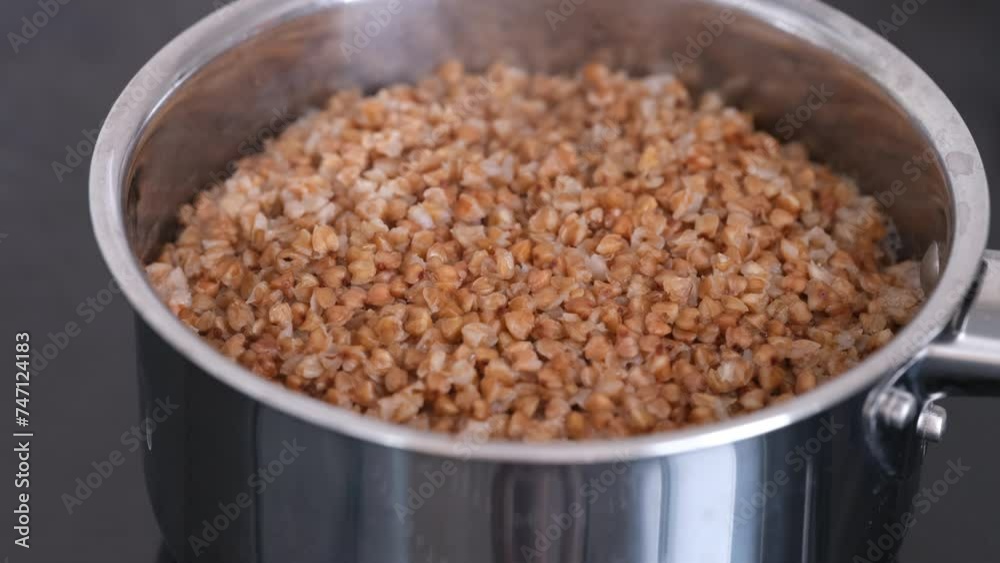 Buckwheat cooking in a steel pot on the black stove top. Close-up. Buckwheat cooking in a steel pot on the black stove top. Close-up.