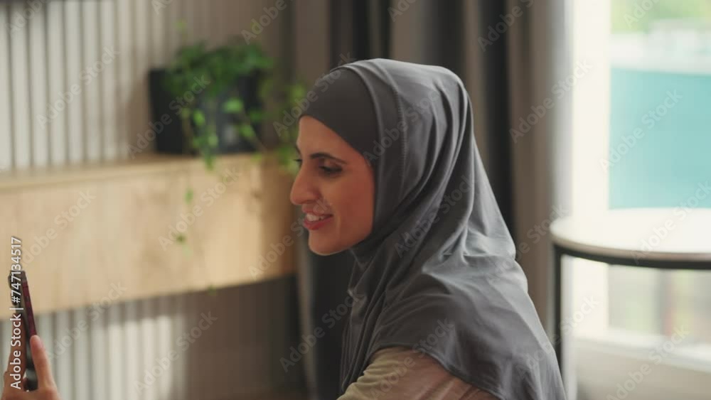 Smiling Arab woman having online video call on cellphone, waving hand on camera Smiling Arab woman having online video call on cellphone, waving hand on camera