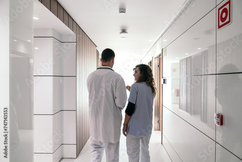 Photos Rear view of healthcare workers in dialogue in hospital corridor.