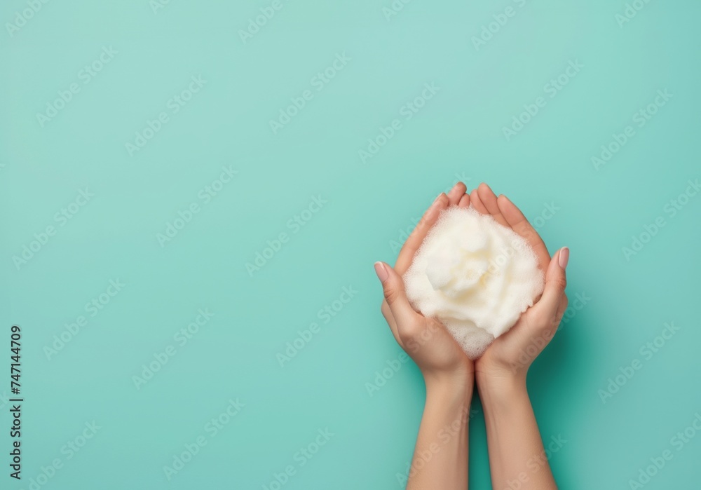 Womans hands cradles a mound of fluffy white soap foam against a turquoise background - obrazy, fototapety, plakaty 