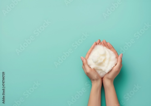 Womans hands cradles a mound of fluffy white soap foam against a turquoise background