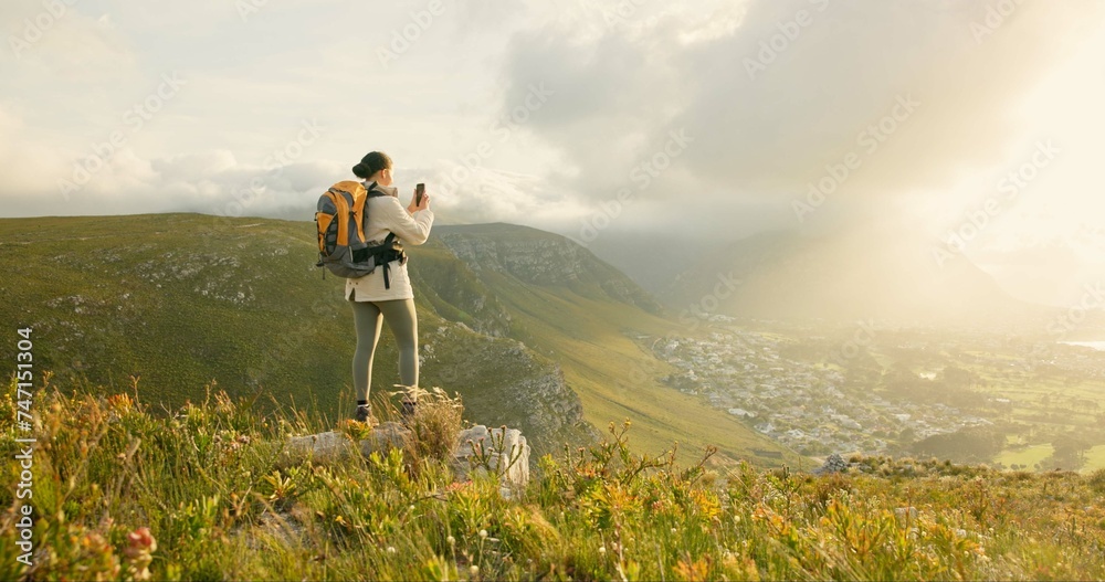 Woman, hiking and video recording on mountains in adventure, wellness and health with nature and cityscape. Person with backpack and trekking photography on green hill, travel or eco friendly journey - obrazy, fototapety, plakaty 