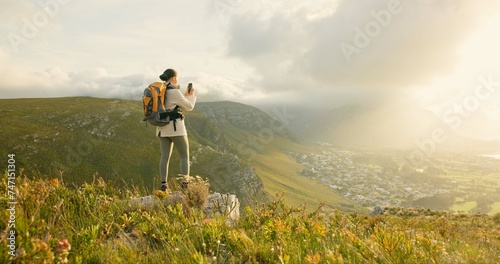 Woman, hiking and video recording on mountains in adventure, wellness and health with nature and cityscape. Person with backpack and trekking photography on green hill, travel or eco friendly journey photo