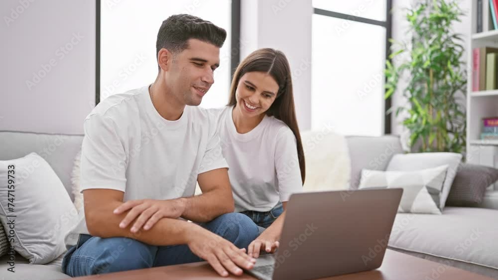 A smiling couple using a laptop together in a modern living room, depicting intimacy and technology in a home setting. A smiling couple using a laptop together in a modern living room, depicting intimacy and technology in a home setting.