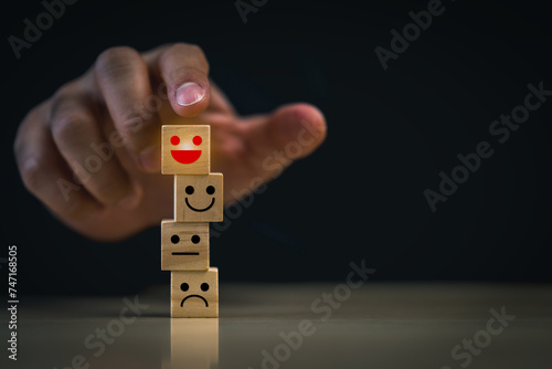 Hand Stacking Emotional Expression Blocks. A hand is stacking wooden blocks with various emotional faces, symbolizing the management of emotions. Symbol of customer satisfaction concept.