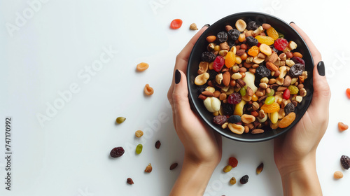 Woman hand holding bowl filled with mix dryfruits on white background, dry fruits around