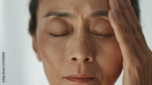 A woman with closed eyes pressing her hands against her temples conveying a sense of stress or discomfort.