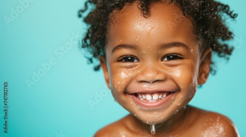 A joyful child with water droplets on their face smiling brightly against a teal background.
