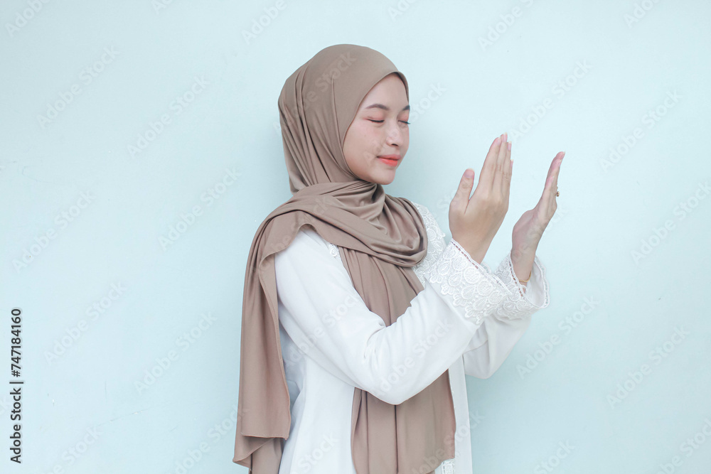 Religious Young Asian Muslim woman wearing hijab praying to God. Isolated in gray background. Religious Young Asian Muslim woman wearing hijab praying to God. Isolated in gray background.