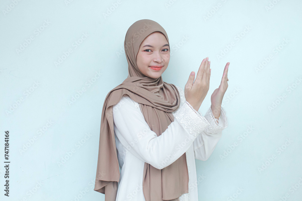 Religious Young Asian Muslim woman wearing hijab praying to God. Isolated in gray background. Religious Young Asian Muslim woman wearing hijab praying to God. Isolated in gray background.