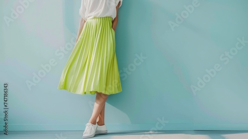 A woman in a vibrant lime green midi skirt and white top standing against a light blue wall with her legs crossed and hands resting on her hips exuding a casual yet chic style.