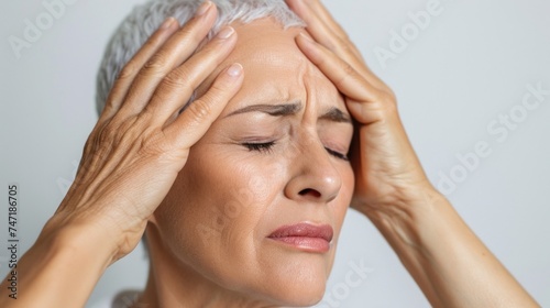 A woman with short hair holding her head in her hands looking distressed with closed eyes.