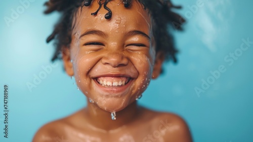 A joyful child with water droplets on their face smiling broadly with eyes closed against a blue background. photo