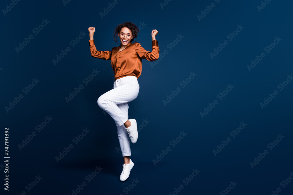 Full length photo of lovely young lady jump excited winner dressed stylish brown silk formalwear isolated on dark blue color background