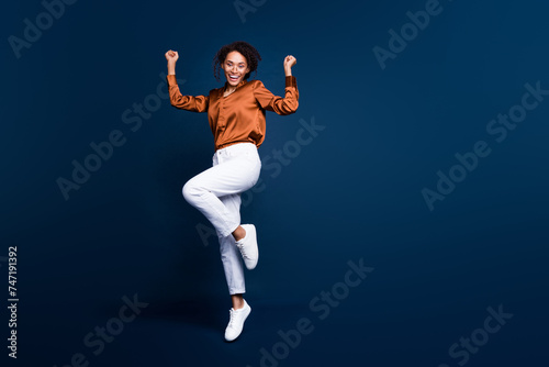 Full length photo of lovely young lady jump excited winner dressed stylish brown silk formalwear isolated on dark blue color background