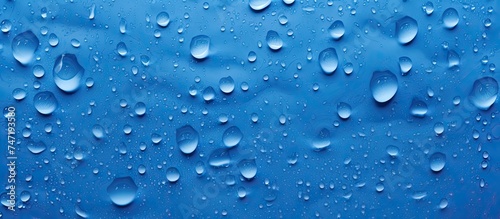 Multiple water droplets are scattered across a blue plastic surface, reflecting light and creating small puddles. The droplets appear round and clear, contrasting against the smooth texture of the