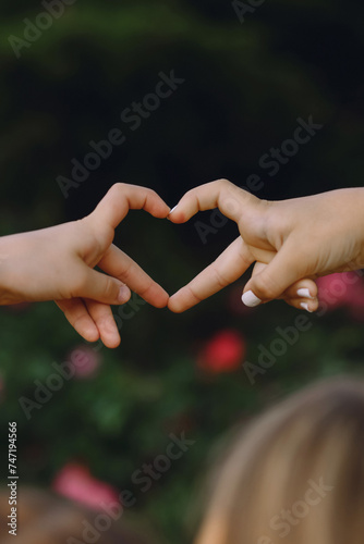 Two little girls make the shape of heart with their fingers on nature background at summer.