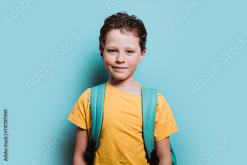 A happy young boy with a backpack smiles against a turquoise background, exuding confidence and excitement for school