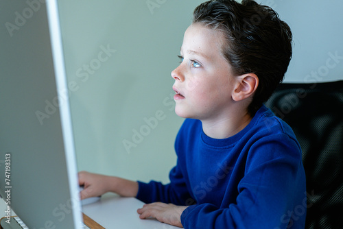 A young boy with a look of concentration while using a computer in a home environment, potentially engaged in online learning photo