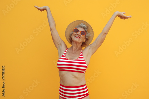 Cool funky elderly Latin American woman dressed striped red swimsuit dancing having fun isolated yellow color background photo