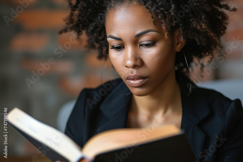 Focused African American business woman reading a book in office closeup.