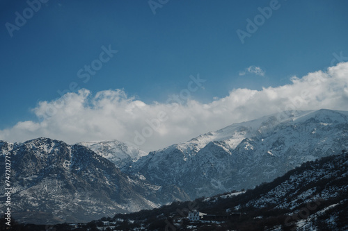 Panoramic view of snow-capped mountains against a blue cloudy sky.