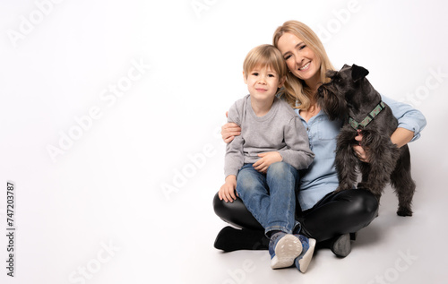 Beautiful young mother with child boy and puppy schnauzer dog sitting on floor on white background