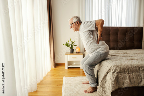 A senior man is trying to get up from a bed with his painful backs. © dusanpetkovic1