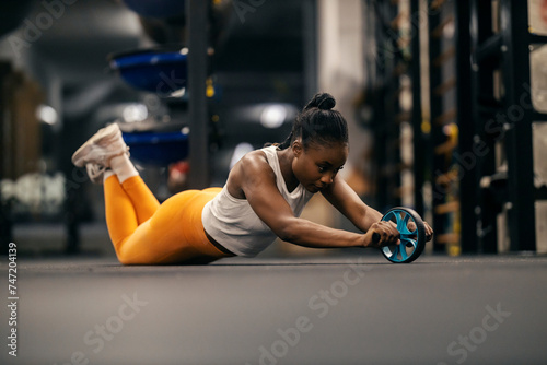 A dedicated fit black sportswoman doing workouts with ab roller at gym. photo