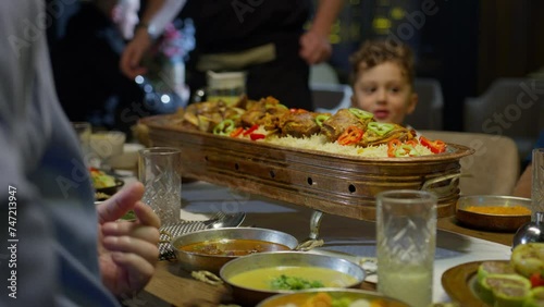 A waiter serves a boat-shaped plate full of rice, peppers and meat on a table in front of a Muslim family on the occasion of Ramadan or Eid photo