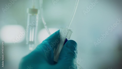 In the office, doctor in special clothes carefully adjusts an IV drip. Professional wearing medical gloves installs a modern drip system to treat patients. Injecting medications with a needle and tube
