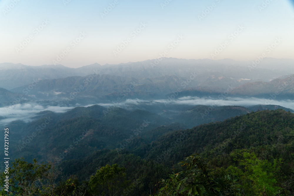 Misty mountain landscape, clear blue cloudless sky and layers of hills. Cold mood.