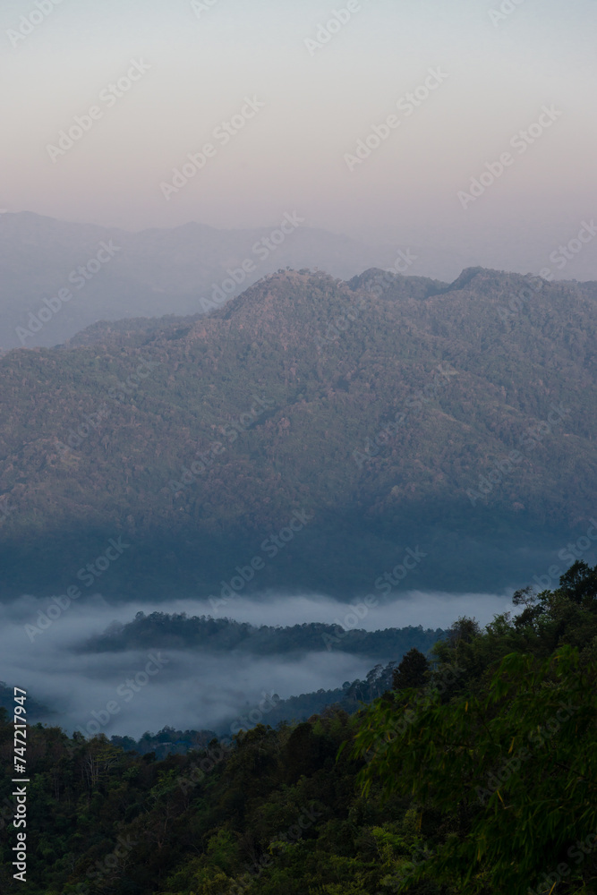 Misty mountain landscape, clear blue cloudless sky and layers of hills. Cold mood.