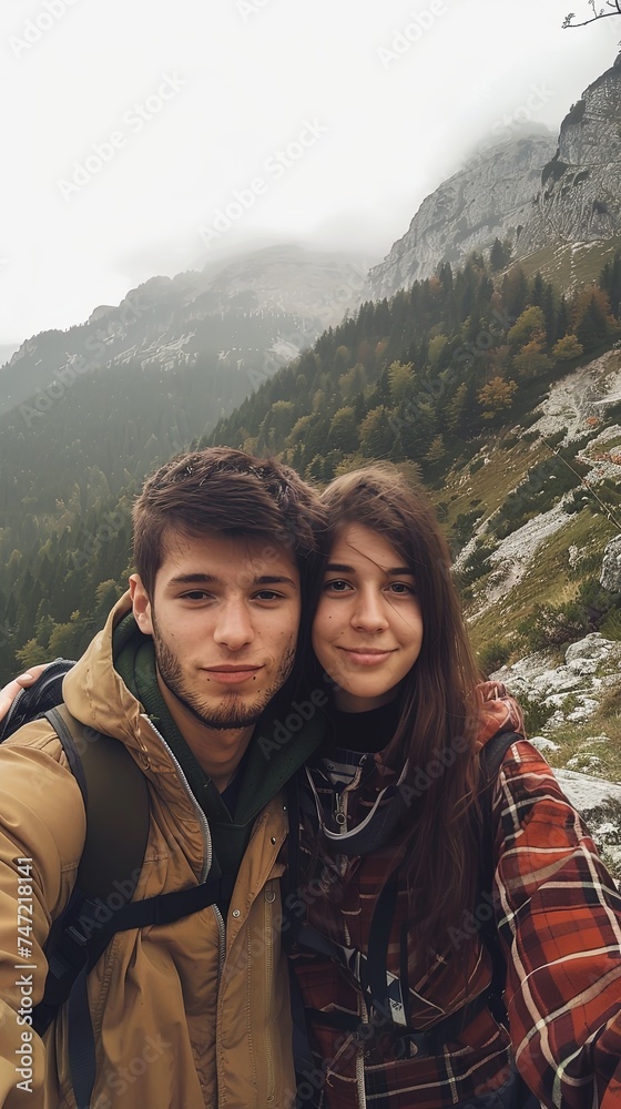 Vertical portrait of young happy man and woman on a mountain taking selfie