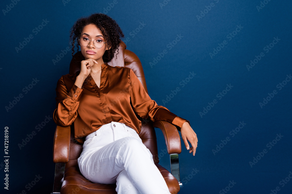 Photo portrait of lovely young lady sit office serious manager wear trendy brown satin formalwear isolated on dark blue color background Photo portrait of lovely young lady sit office serious manager wear trendy brown satin formalwear isolated on dark blue color background