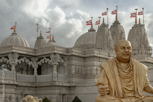 The gold colored statue of spiritual leader holiness pramukh swami maharaj front of Neasden temple (BAPS Shri Swaminarayan Mandir) against a nice cloudy sky background. Hindu temple in Neasden to buil photo