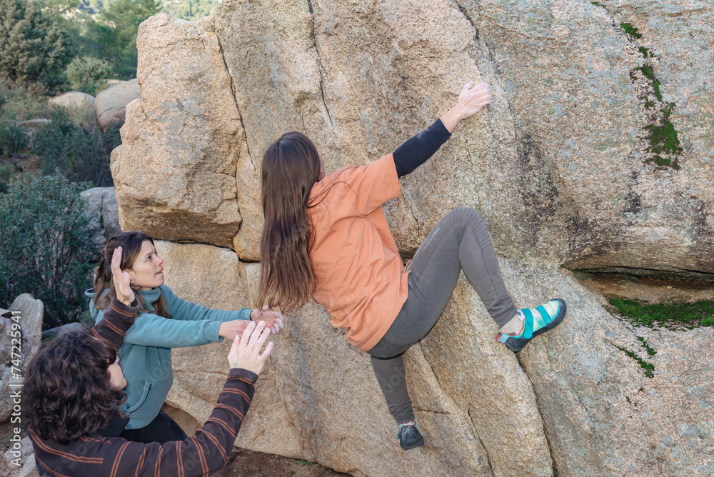 © ADDICTIVE STOCK - A climber reaches for a high hold, supported by attentive teammates, amidst a rugged granite boulder landscape