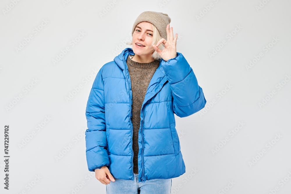 Smiling woman in winter clothes gesturing with hands on a gray background. Smiling woman in winter clothes gesturing with hands on a gray background.
