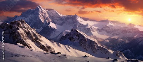 The sun is descending below the horizon, casting a warm glow over the snow-covered peaks of the Bucegi Mountains. The sky is painted in hues of orange and pink as the night begins to settle in.