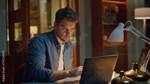 Serious accountant texting laptop night home closeup. Focused man writing notes photo