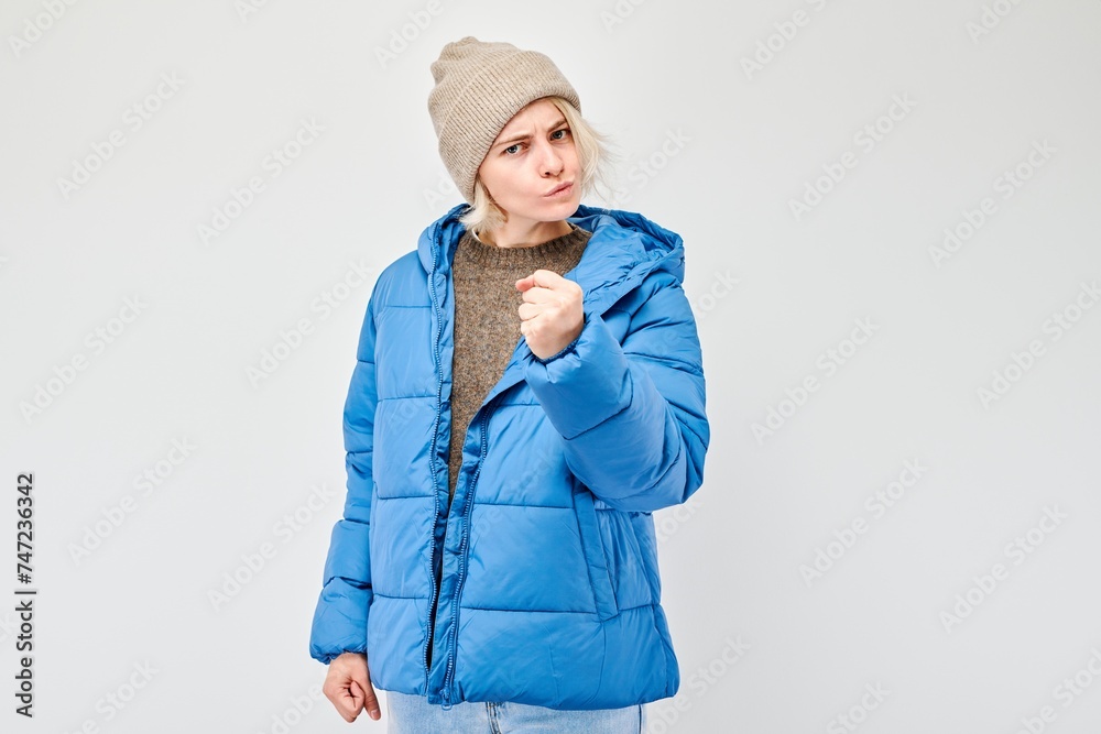 Woman in winter attire screams with anger threatens with fist against a white background. Woman in winter attire screams with anger threatens with fist against a white background.