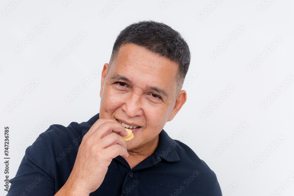 A middle aged asian man munches on a biscuit. Having a quick snack, posing on a white background. A middle aged asian man munches on a biscuit. Having a quick snack, posing on a white background.